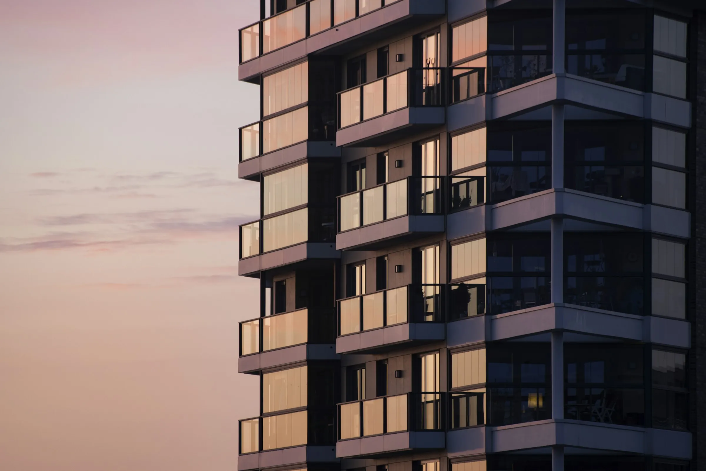 Modern apartment tower with glass balconies against a soft sunset sky