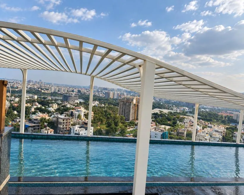 Rooftop infinity pool under a white pergola with city views at Premia, Jakkur